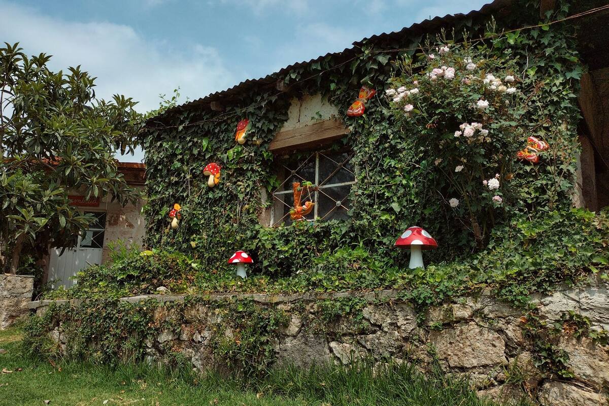 Un edificio rústico con muros cubiertos de hiedra y decoraciones colgantes con forma de seta.