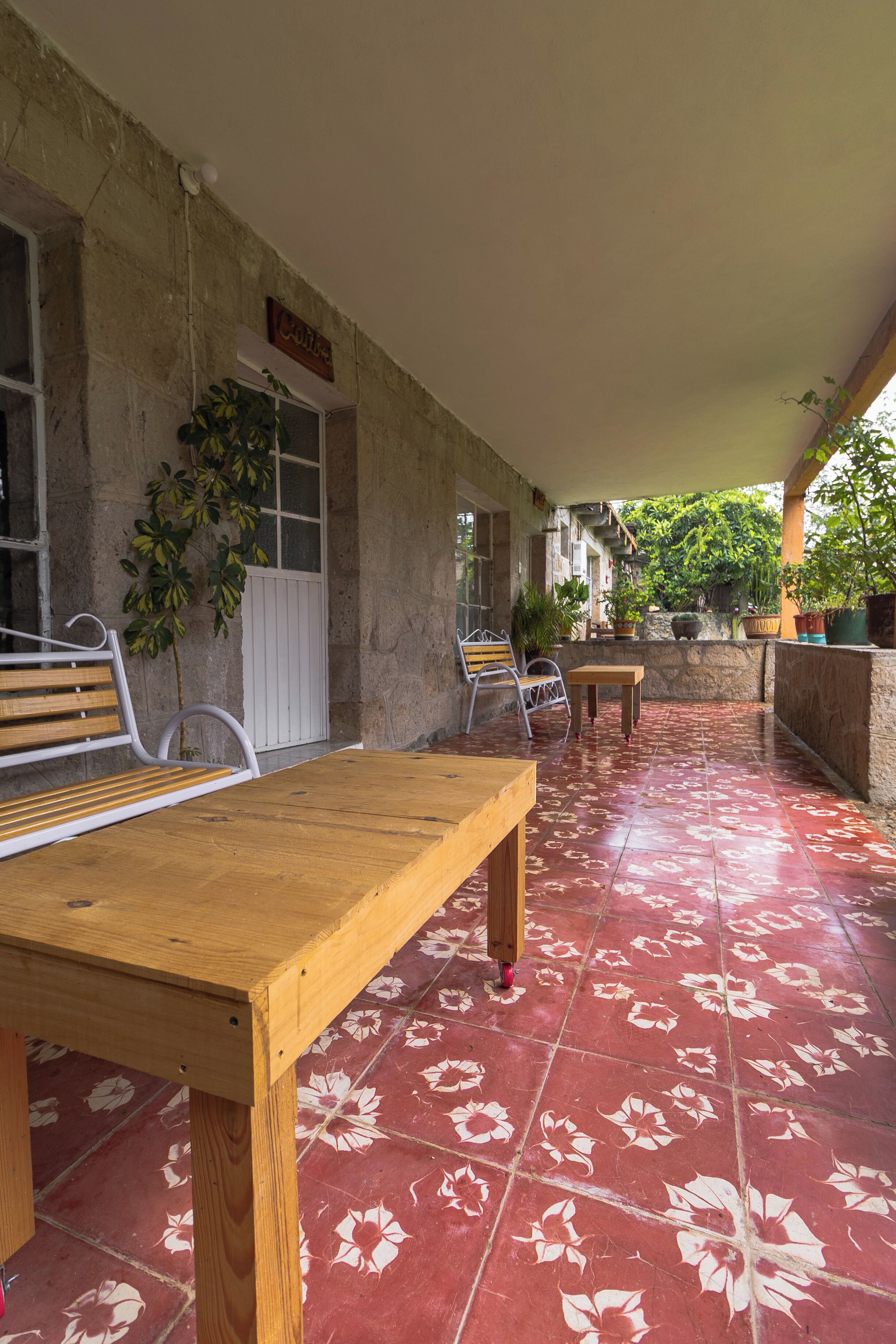 Une terrasse couverte avec une table et des chaises en bois, un banc et des plantes en pot.
