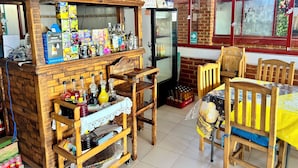 Een houten kiosk in rustieke stijl met een koelkast, planken vol diverse artikelen en een tafel met stoelen.