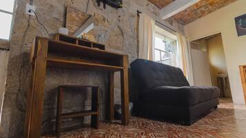 Ein Wohnzimmer mit einer schwarzen Couch, Holzmöbeln, einer Ziegelwand und einem an der Wand befestigten Fernseher.