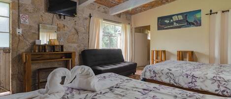Una habitación con dos camas, televisión, pared de piedra y un cuadro.