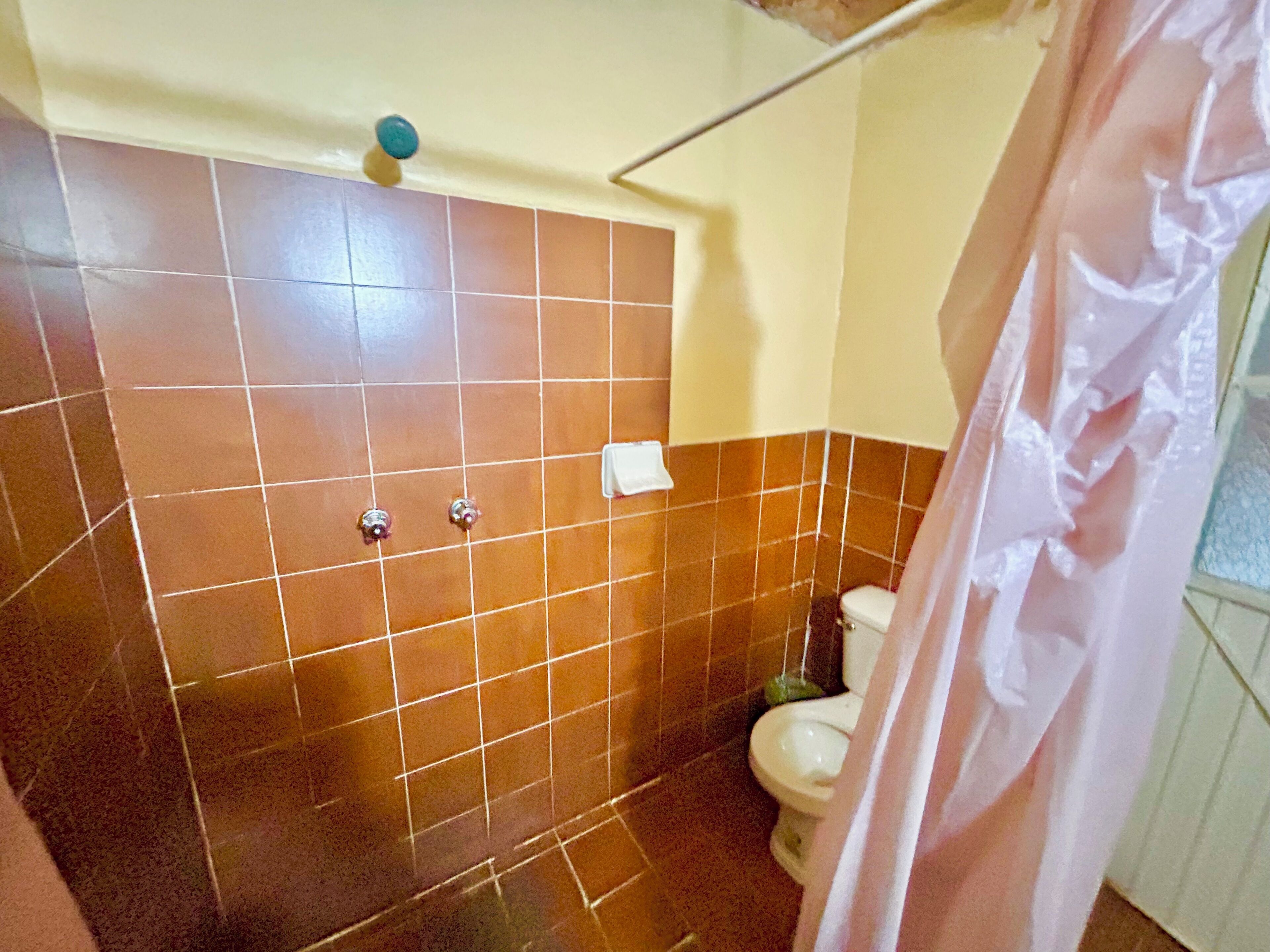 Un baño con azulejos marrones, un inodoro blanco y una cortina de ducha.