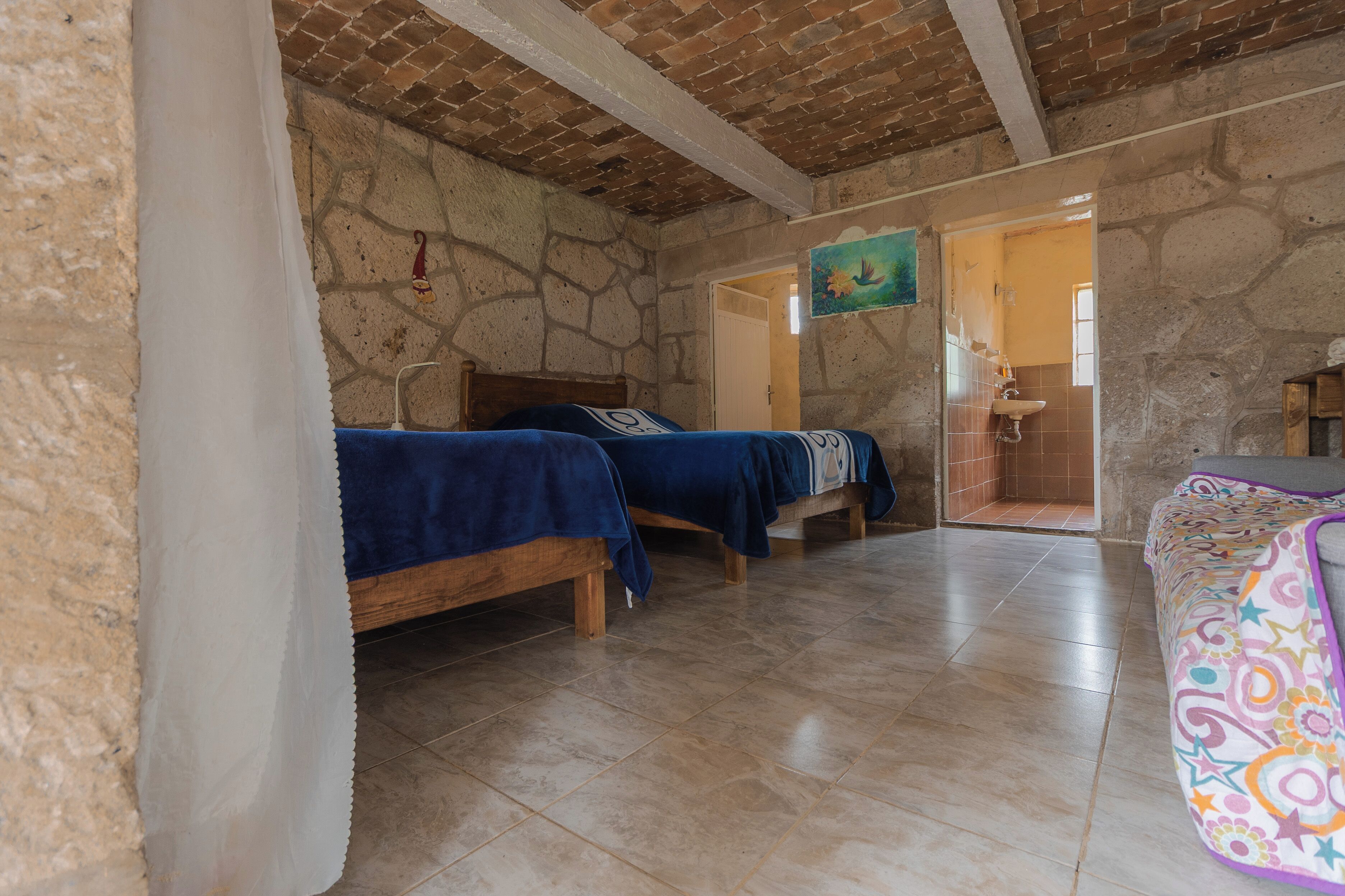 A room with two wooden beds, a bathroom with a sink, and a colorful sofa.