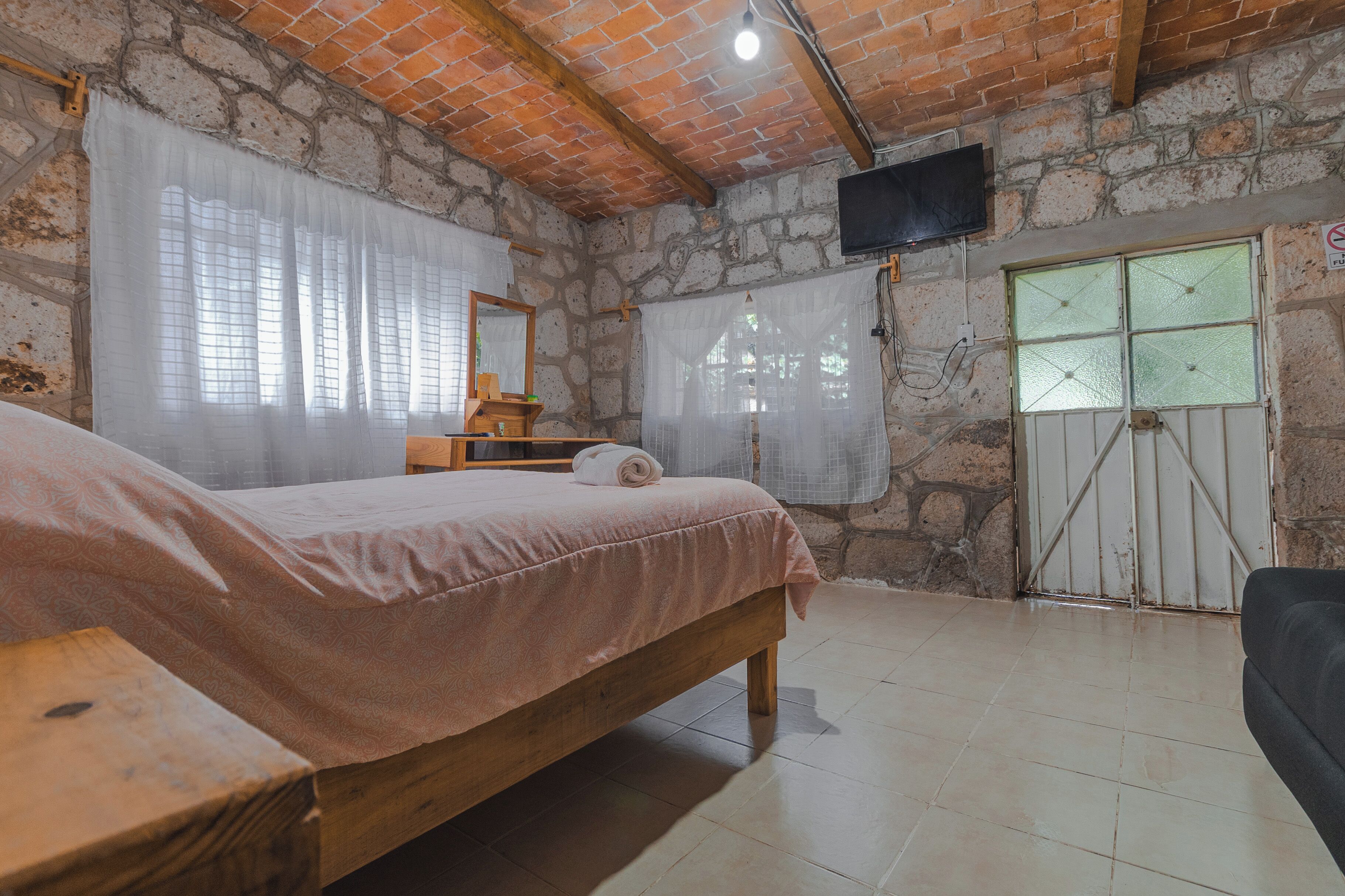Un dormitorio con cama, un banco de madera, un televisor y una pared de piedra.