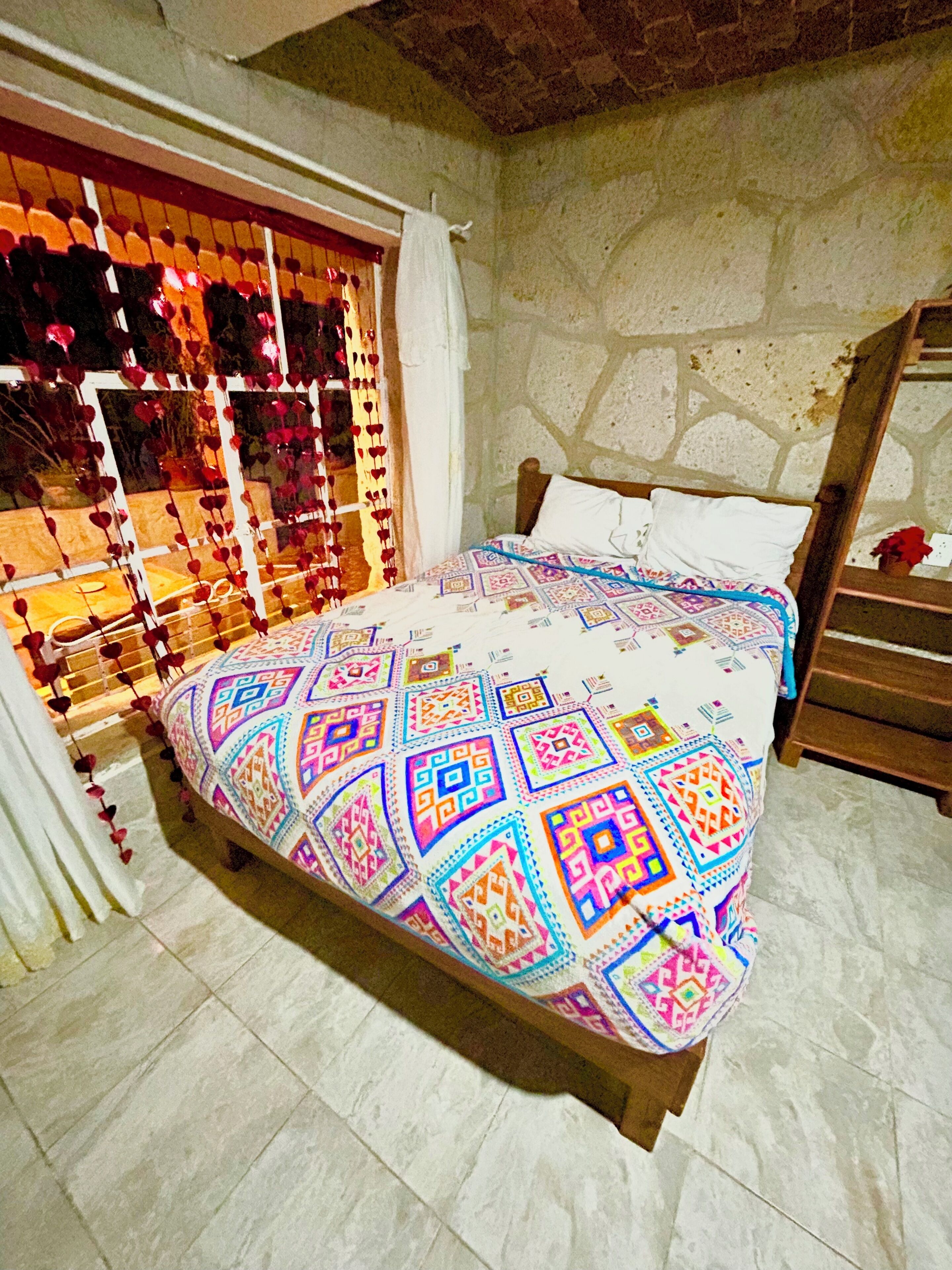 Una cama con una colcha estampada, una pared de piedra y una escalera de madera.