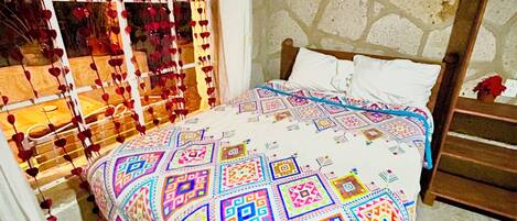 Una cama con una colcha estampada, una pared de piedra y una escalera de madera.