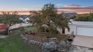 A residential property with a stone wall, a red-roofed structure, and a tree in the yard. - Charming Barndominium with Farm Animals – Just 5 Minutes from Lake Georgetown (Georgetown)