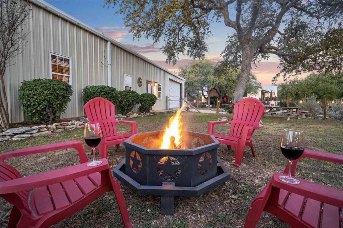 Uma lareira com duas cadeiras Adirondack vermelhas e dois copos de vinho tinto, em um quintal com um edifício ao fundo.