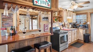 A kitchen with wooden cabinets, a stove, a microwave, and a bar area with stools and wine glasses. - Charming Barndominium with Farm Animals – Just 5 Minutes from Lake Georgetown (Georgetown)