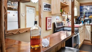 A bar area with a bottle of Bulleit Bourbon and a glass of ice water on a wooden counter. - Charming Barndominium with Farm Animals – Just 5 Minutes from Lake Georgetown (Georgetown)
