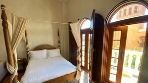 A four-poster bed with a canopy, wooden flooring, and a view of an outdoor courtyard through a glass door. - Apartment in the Historic Center of Cartagena (Cartagena de Indias)