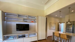 A modern living room with a built-in TV, wooden flooring, and a dining area with bar stools. - Apartment in the Historic Center of Cartagena (Cartagena de Indias)