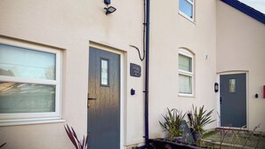 A residential building with a front door, a window, and a small garden area with potted plants. - Ddwylig Bach - UK48623 (Rhyl and Prestatyn)