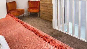 A bedroom with a bed, a wooden dresser, an orange chair, and a television on the wall. - Ddwylig Bach - UK48623 (Rhyl and Prestatyn)