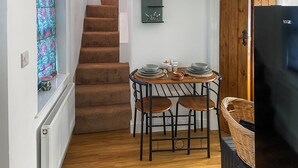 A compact kitchen with a wooden table, two chairs, a black refrigerator, and a staircase leading to another room. - Ddwylig Bach - UK48623 (Rhyl and Prestatyn)