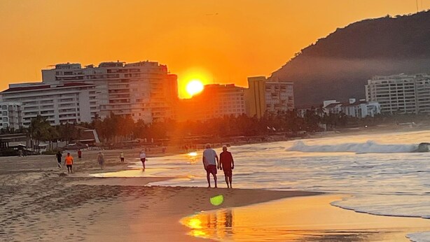 A beach scene with people walking and standing near the water during sunset. - Raya apartment  (Ixtapa Zihuatanejo)