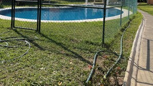 A fenced swimming pool with a clear blue water surface, surrounded by grass and a chain-link fence. - Raya apartment  (Ixtapa Zihuatanejo)
