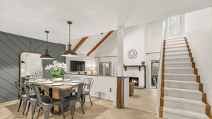 Un comedor espacioso con techo alto, vigas de madera a la vista y una cocina moderna al fondo.