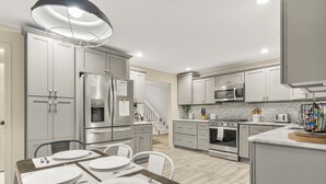 Una cocina moderna con electrodomésticos de acero inoxidable, armarios blancos y una zona de comedor preparada para cuatro.