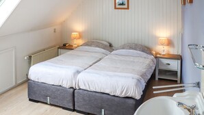 Un dormitorio con cama, mesitas de noche, lámparas, un radiador, un cuadro en la pared y un baño con lavamanos y espejo.