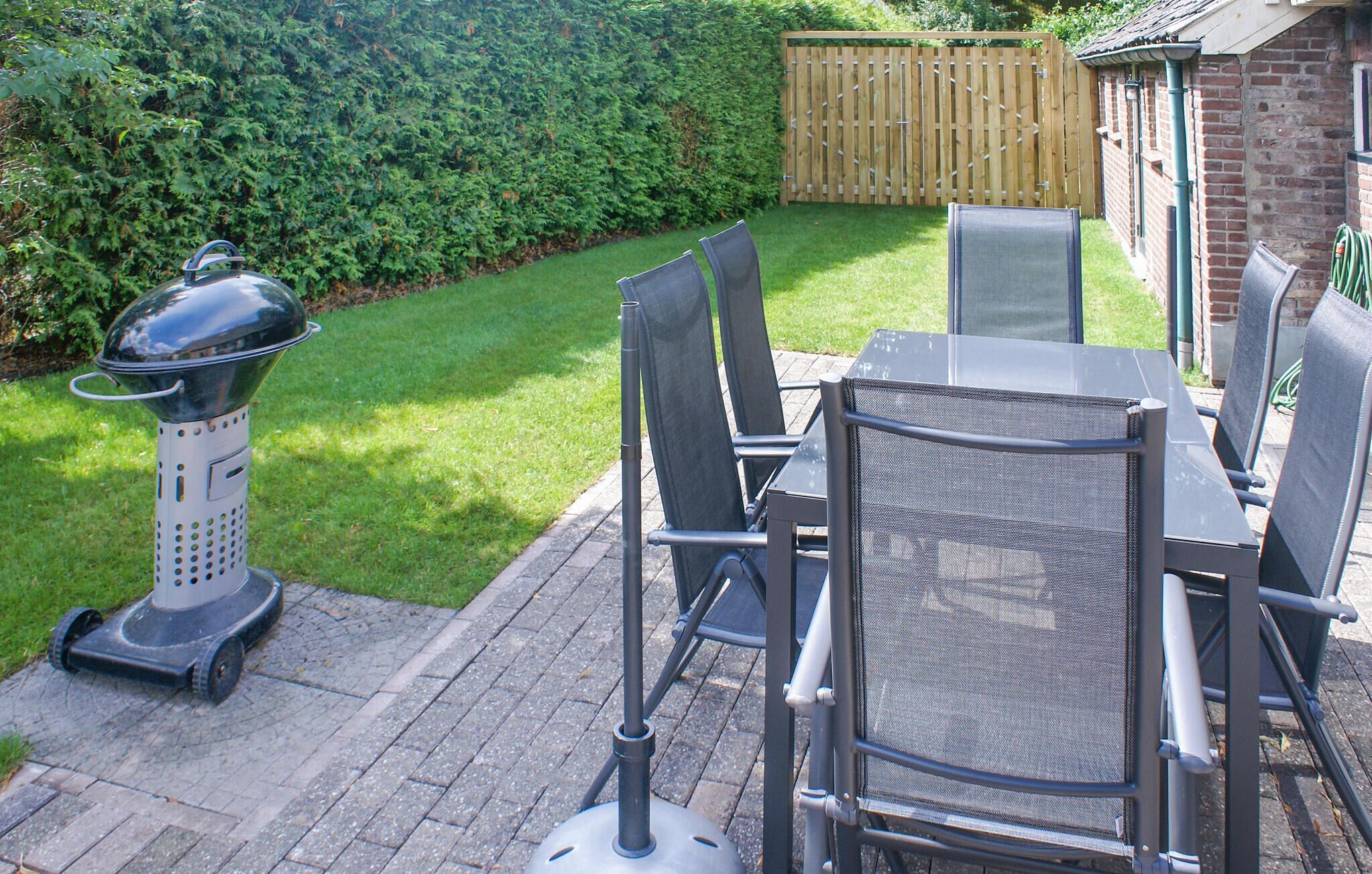 Een terras met een tafel, stoelen, een barbecue en een haag op de achtergrond.