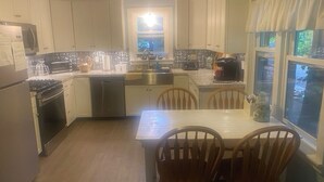 A kitchen with white cabinets, a stainless steel sink, a dining table with four chairs, and a window with curtains. - Angola on the Lake Beach Front House  4BR  private beach wrap-around porches (Angola)