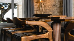 A wooden chair with a curved backrest and cushioned seat, placed at a table with a dark wooden top and a metal base. - Ionian Stone Luxury Villa Aether (Corfu)