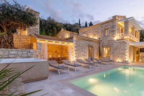 A stone villa with a swimming pool, outdoor seating, and a well-lit patio area. - Ionian Stone Luxury Villa Aether (Corfu)