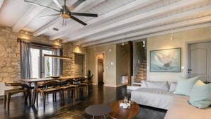 A spacious living area with a stone wall, wooden furniture, and a ceiling fan. - Ionian Stone Luxury Villa Aether (Corfu)
