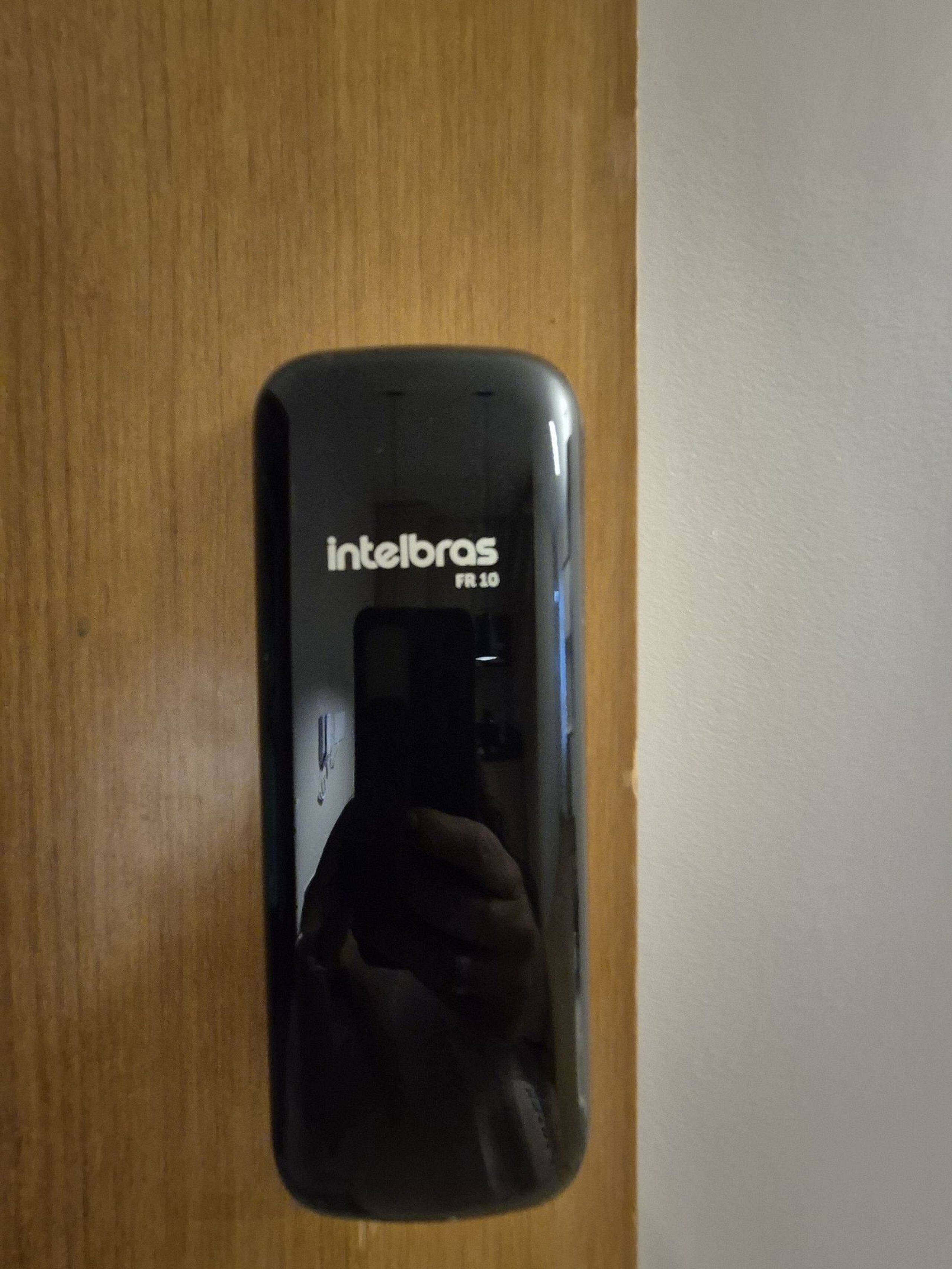 A black smartphone with 'Intelbras FR 10' written on it, placed on a wooden surface.