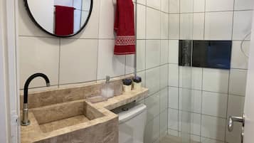 A bathroom with a beige marble sink, a round mirror, a red towel, and a glass shower enclosure.
