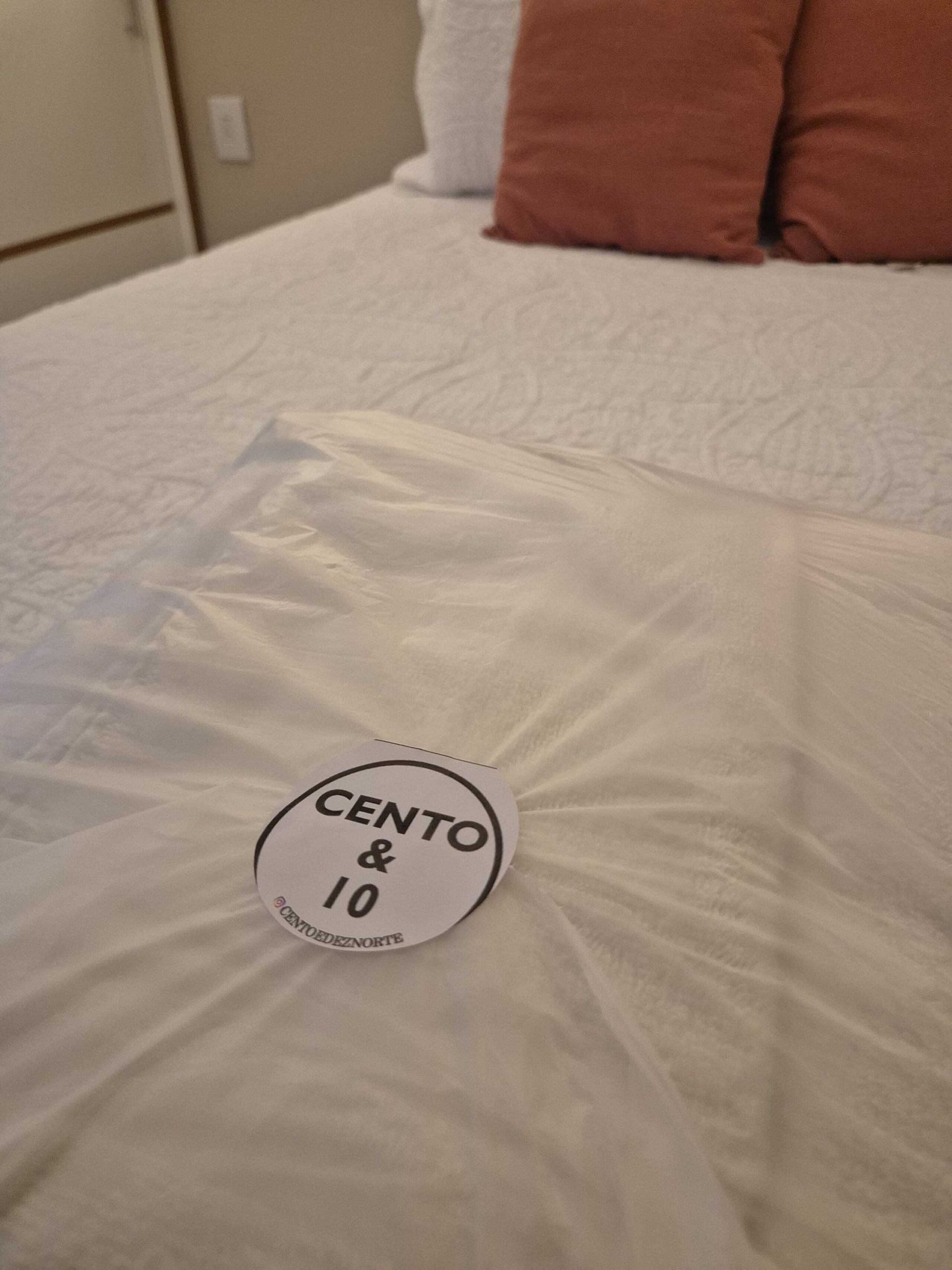A bed with a white comforter and a circular sticker on the bedspread.