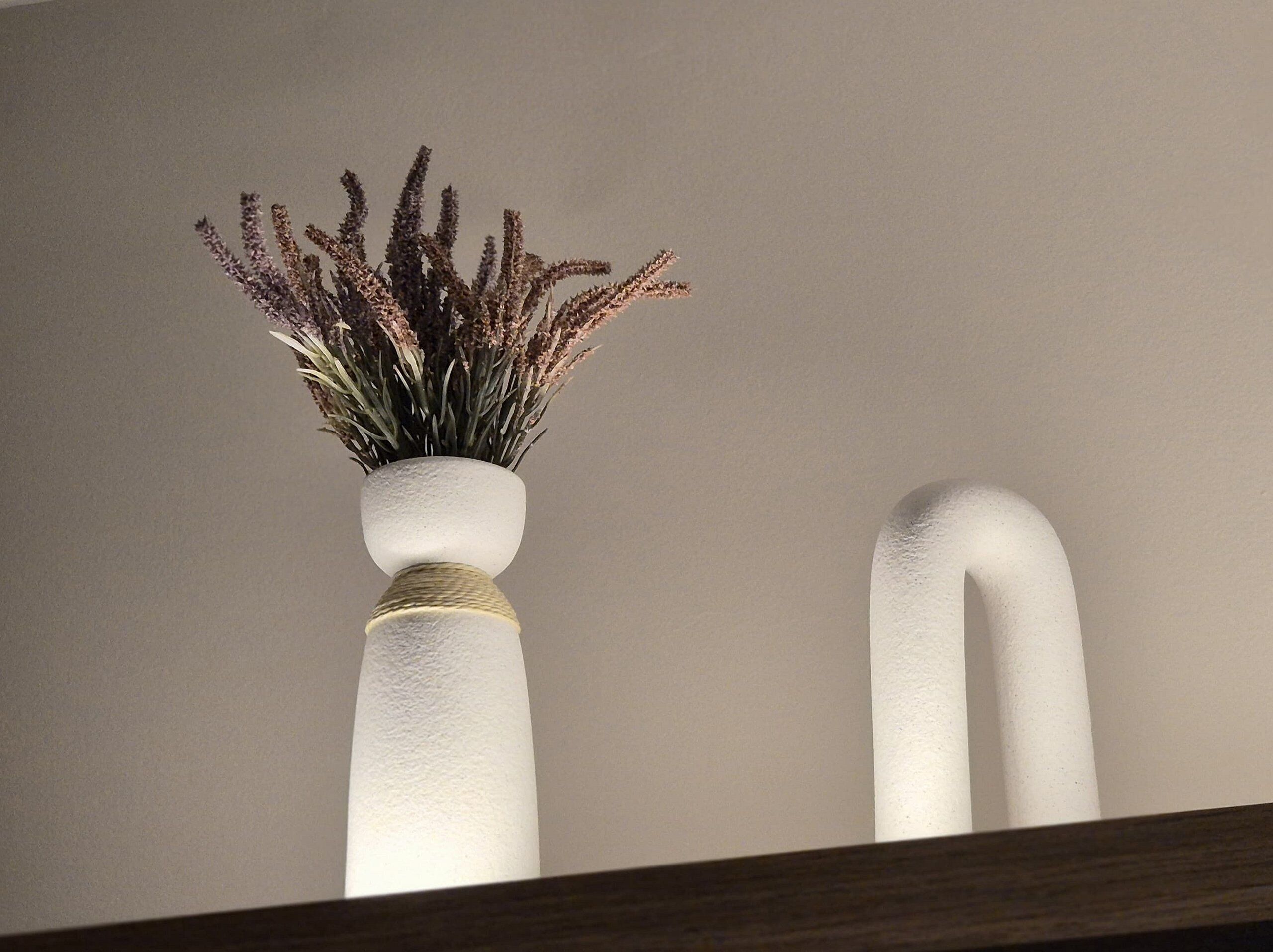 Twee witte vazen met een reliëf oppervlak en touwdetail, geplaatst op een houten ondergrond tegen een effen muur.