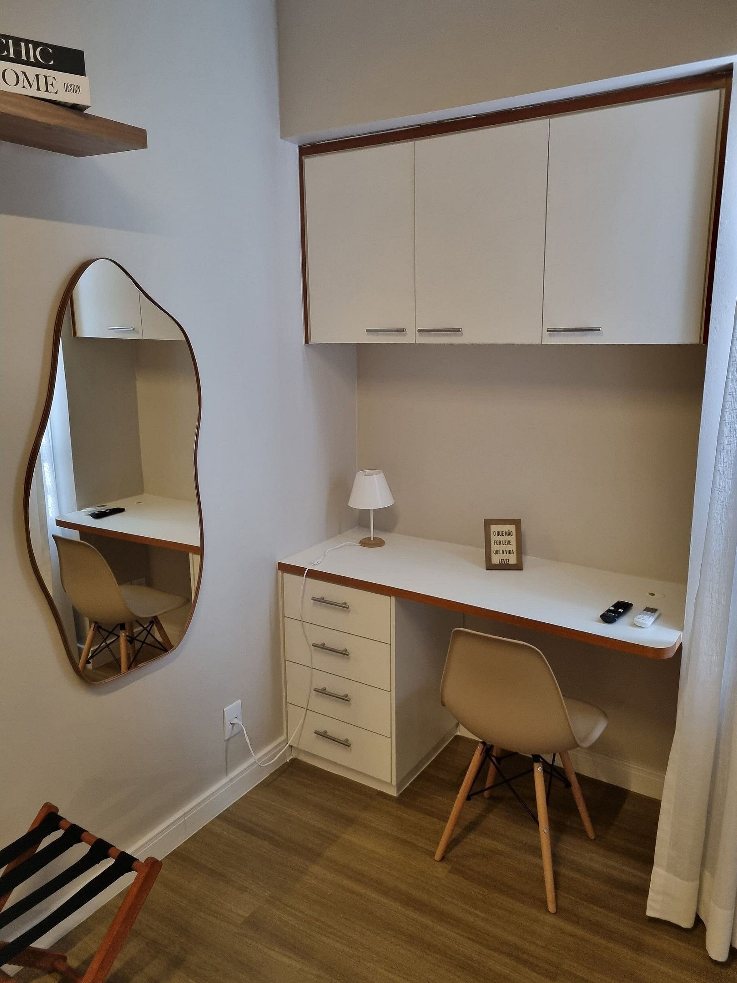 A compact bedroom with a single bed, a desk with a chair, a bedside table, and a mirror.