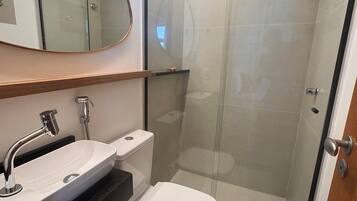 A modern bathroom with a glass-enclosed shower, a white toilet, and a large oval mirror above the sink.