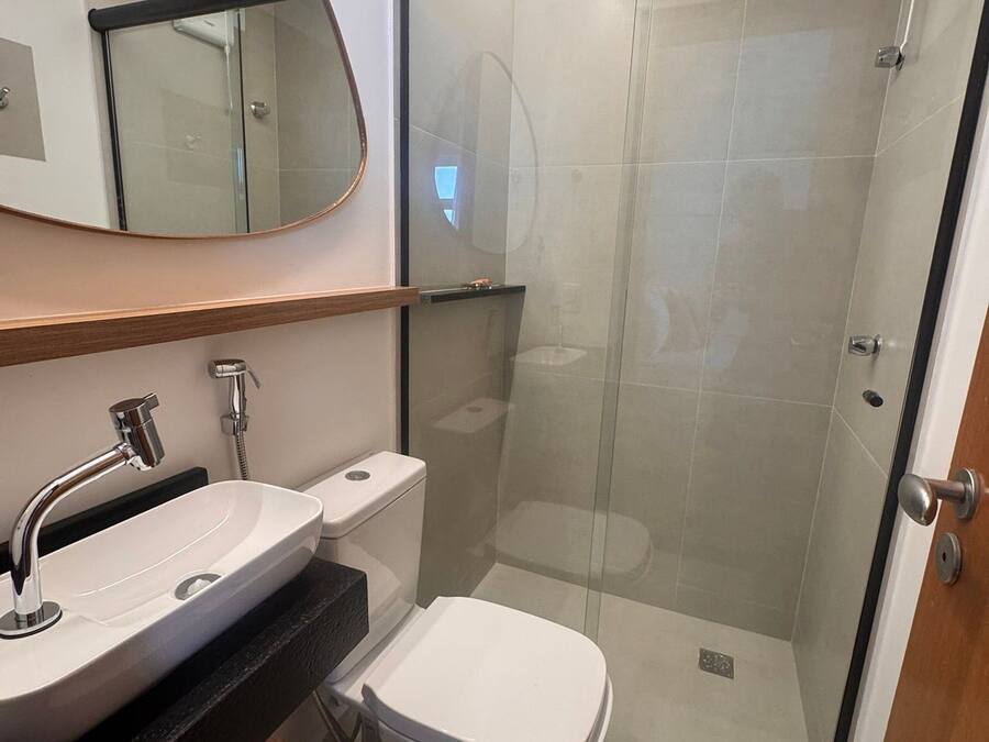 A modern bathroom with a glass-enclosed shower, a white toilet, and a large oval mirror above the sink.