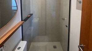 A compact bathroom with a glass-enclosed shower, a toilet, and a vanity with a mirror.