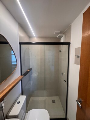 Une petite salle de bain dotée d’une douche à parois de verre, de toilettes et d’un meuble-lavabo avec un miroir.