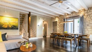 A spacious living area with a wooden staircase, a dining table with chairs, and a large window with curtains. - Ionian Stone Luxury Villas in Corfu - Estate (Corfu)