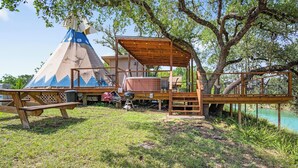 Eine Holzterrasse mit überdachter Sitzgelegenheit, einem Picknicktisch und einer Tipizee-Struktur.