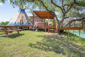 A wooden deck with a covered seating area, a picnic table, and a teepee structure. - Stronghold Retreat | 3 Cabins by Creek w/ Hot Tubs (Bandera)
