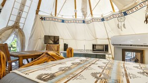 A cozy interior of a tent with a bed, wooden chairs, a table, a television, a microwave, and an air conditioning unit. - Bandera Stronghold Retreat (Bandera)