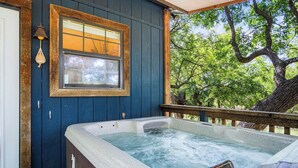Ein Whirlpool mit Holzterrasse, ein Fenster mit Blick auf Bäume und eine Holztür.