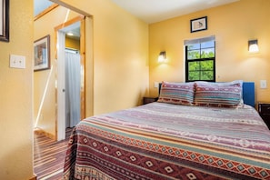 A bedroom with a bed, patterned bedding, a window with a view, and a door leading to another room. - Stronghold Retreat | 3 Cabins by Creek w/ Hot Tubs (Bandera)