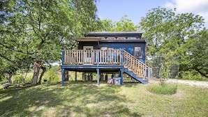 A two-story wooden cabin with a deck and stairs, surrounded by trees and grass. - Bandera Stronghold Retreat (Bandera)