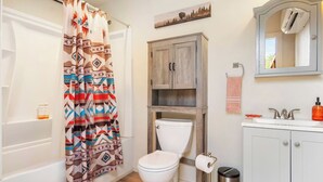 Ein Badezimmer mit Duschvorhang, Toilette, Waschbecken, Schrank und Mülleimer.