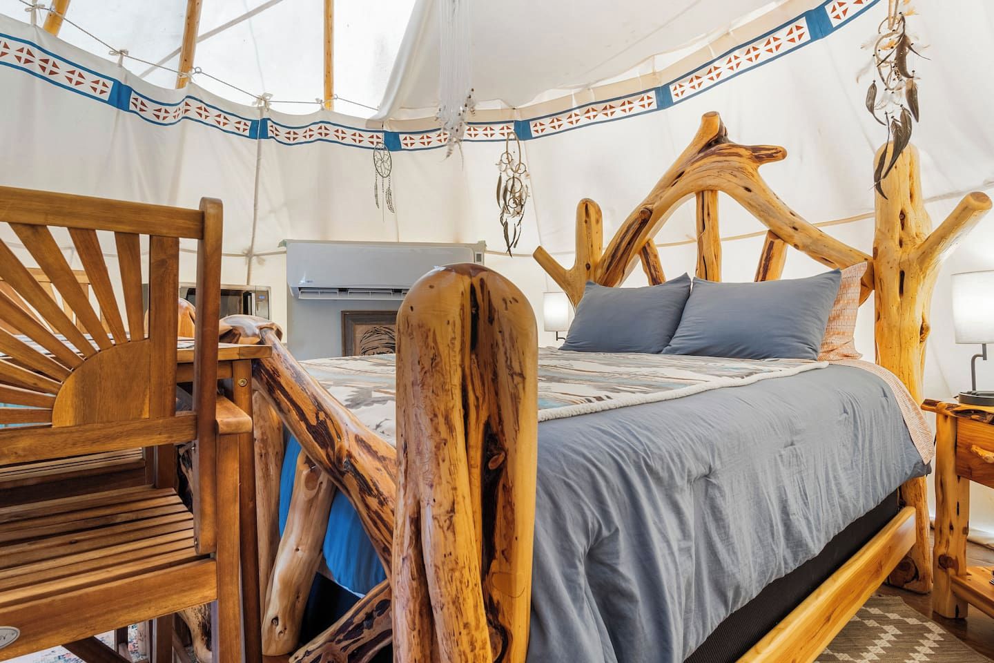 Une tente équipée d’un lit avec une tête de lit en bois, d’un banc et d’un attrape-rêves suspendu.