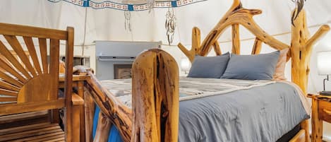 Une tente équipée d’un lit avec une tête de lit en bois, d’un banc et d’un attrape-rêves suspendu.