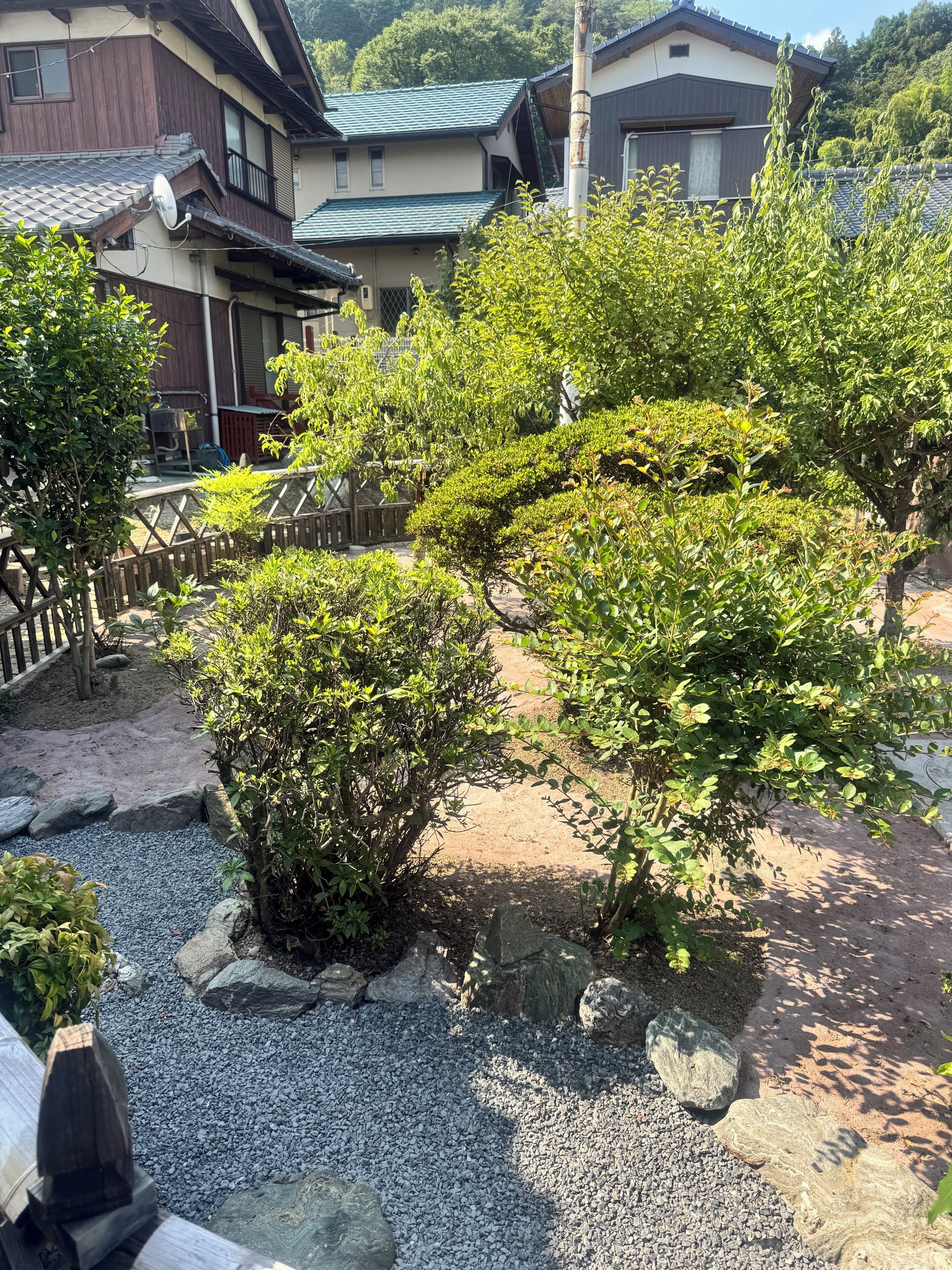 A traditional Japanese garden with a gravel path, rocks, and neatly trimmed bushes.