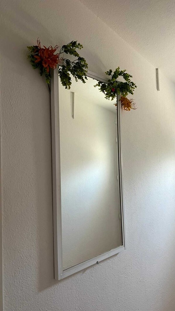 A mirror with a simple white frame mounted on a plain wall.